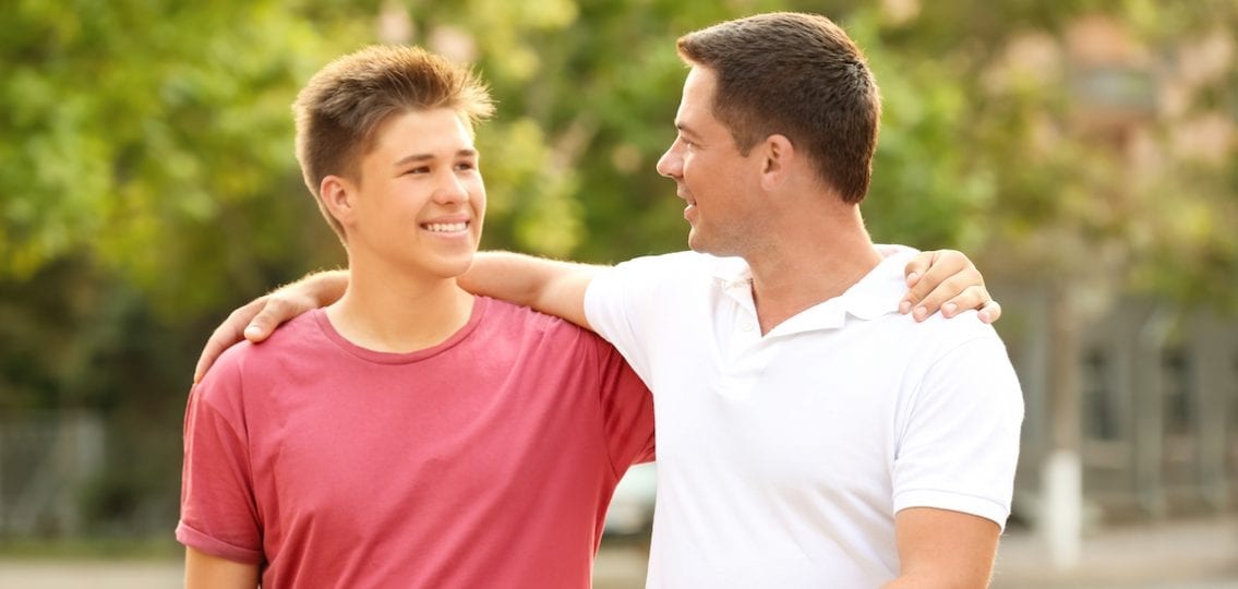 dad and son with arms around each other talking outdoors in a park
