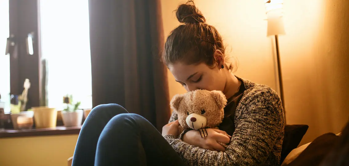 Portrait of a sad teenage girl hugging a teddy bear.