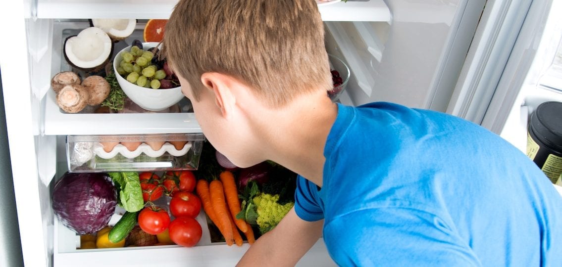 teen looking through a full fridge of vegetables and fruit