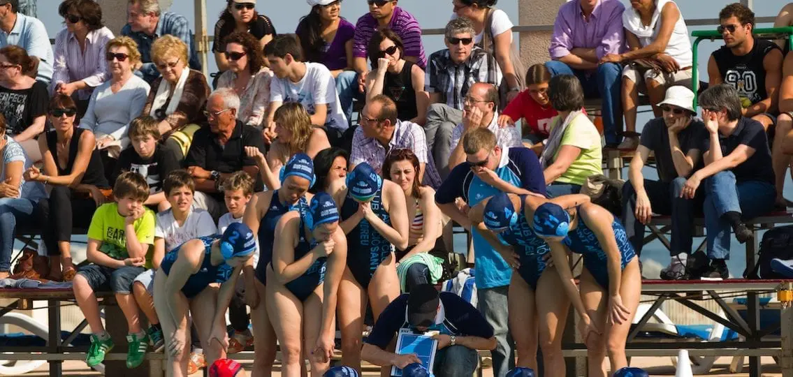 teen girls swim team with coach in front of bleacher full of families