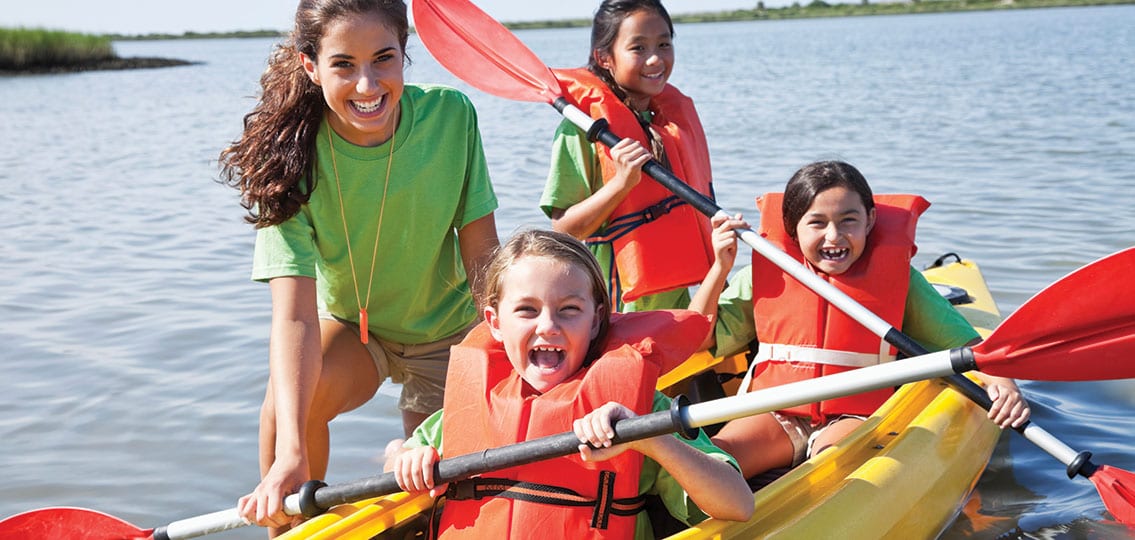 Girls In A Double Kayak with a teen camp counselor smiling and laughing