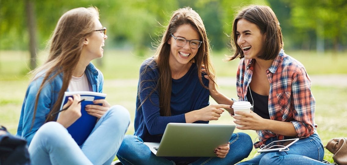 three college girls smiling and laughing and studying outside