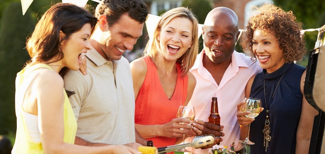 group of parents who are friends at a barbecue smiling and drinking together