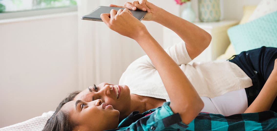 Mother And Daughter Laying On Bed Using Digital Tablet