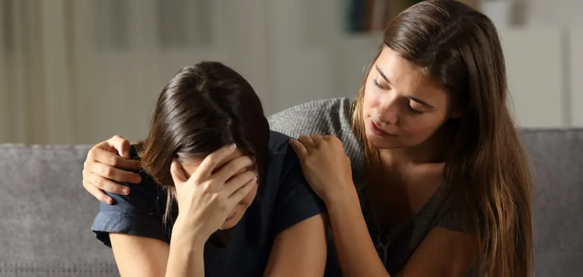 depressed teen girl crying while another girl comforts her on the couch
