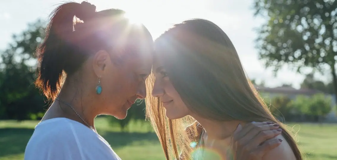 happy mom and teen daughter touching foreheads framed by sun