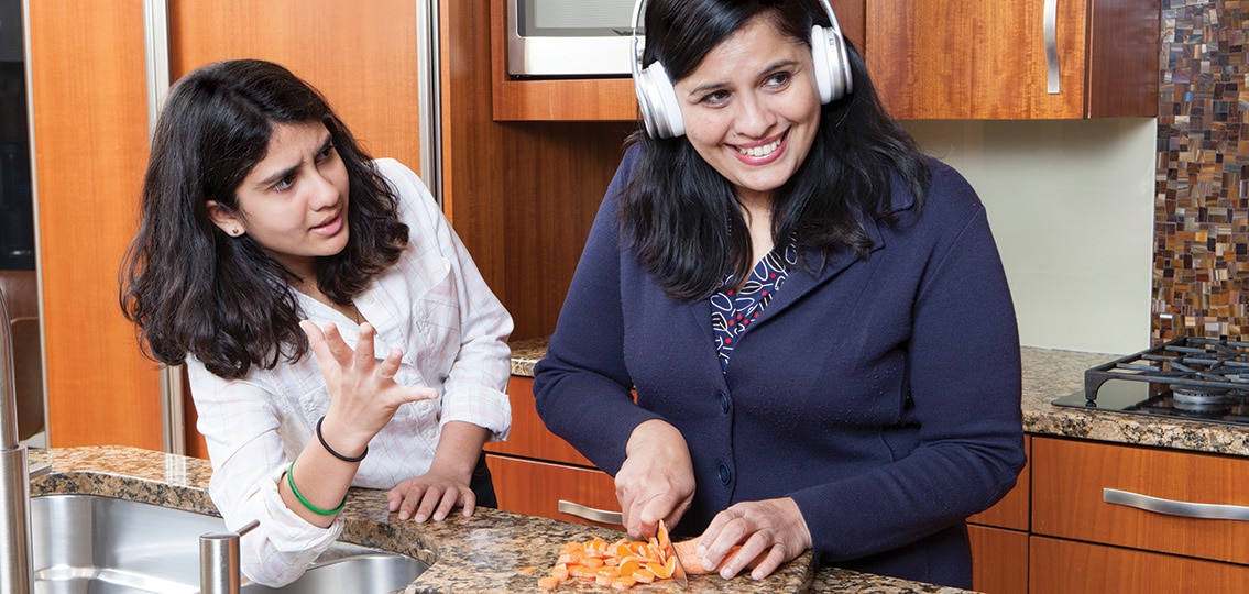 Mom ignoring daughter with headphones while cutting carrots