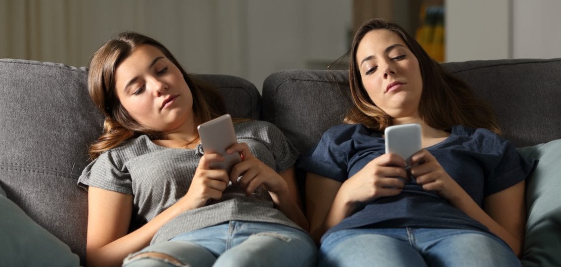 two teen girls texting on the couch looking bored