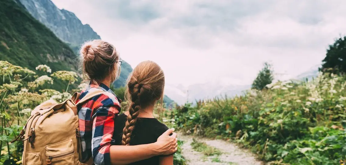 family traveling moms arm over teen daughter's shoulder in some mountains