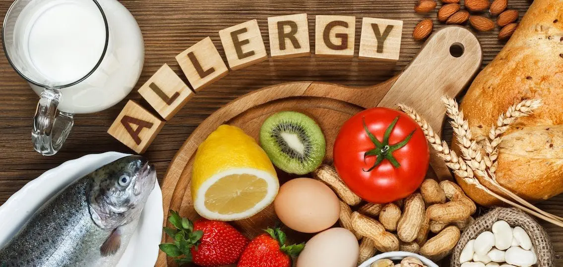 the word allergy spelled out with wooden blocks surrounded by common food allergies such as peanuts and fish