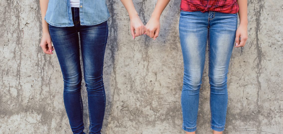 Teen girls holding hands in front of stone wall