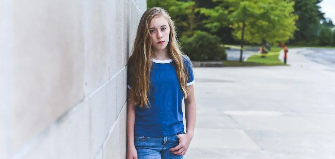 Angry seventh grader leaning against school wall outside