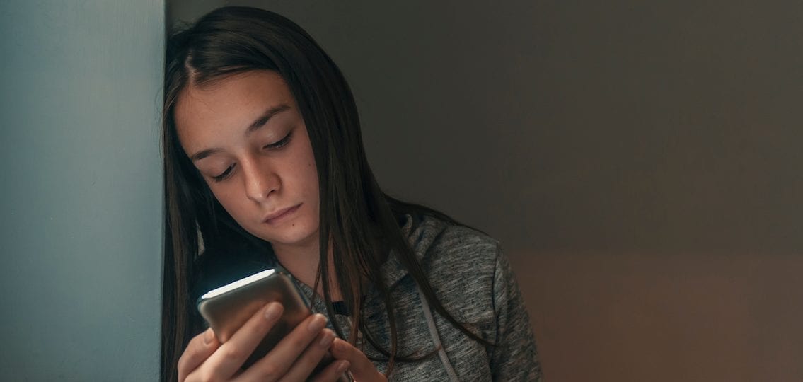 Stressed young teen on phone in dark room