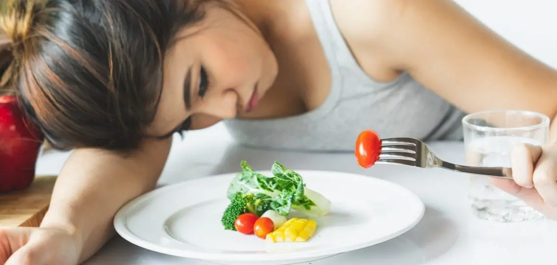 Teenager with eating disorder looking at a plate of vegetables