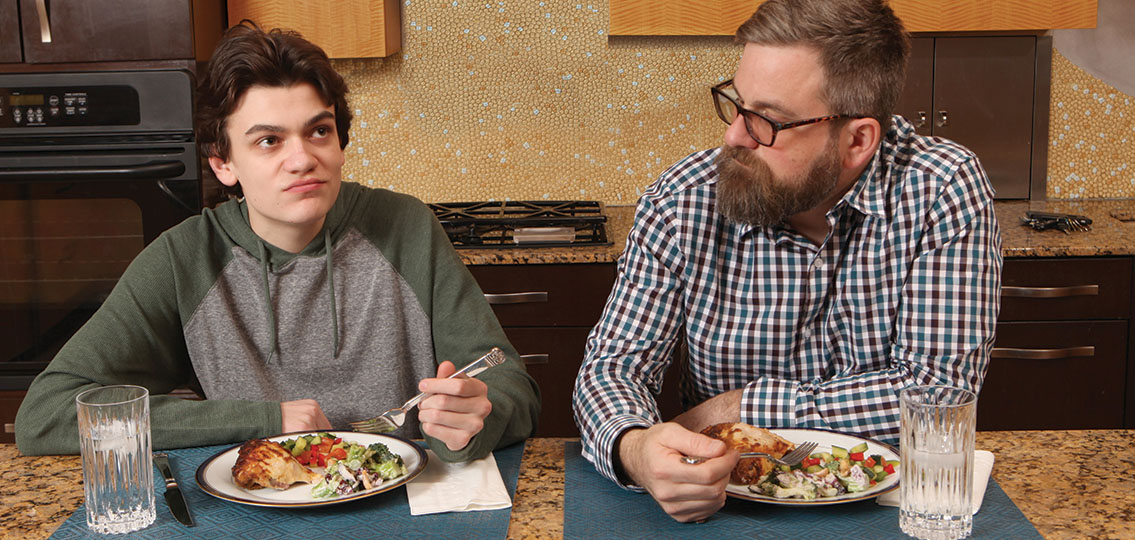 Dad and teen son eating dinner together in kitchen
