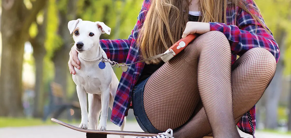 Close-up of legs of teenage girl on skateboard with her dog