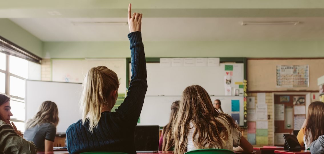 Teen girl speaking up in class raising her hand from back of the room