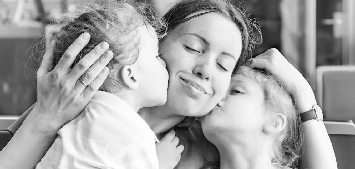 happy smiling Mom with two young kids kissing her cheeks black and white