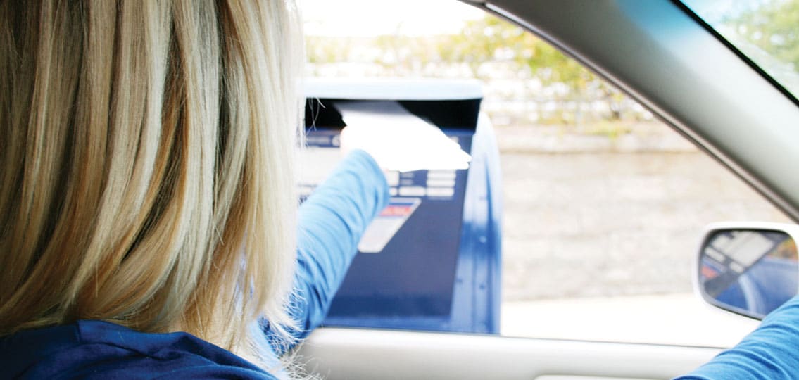Woman mailing a letter from her car putting envelope into mailbox