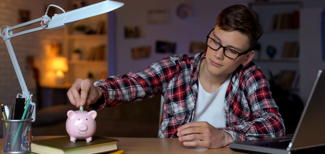 Teen boy saving money in piggybank in room