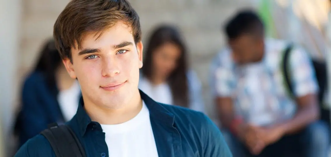 teenage boy close up smiling at the camera with blurred teens behind him
