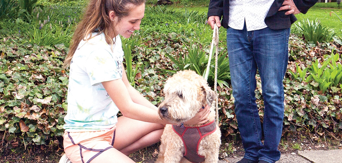 teenage Girl petting dog while owner stands in the background