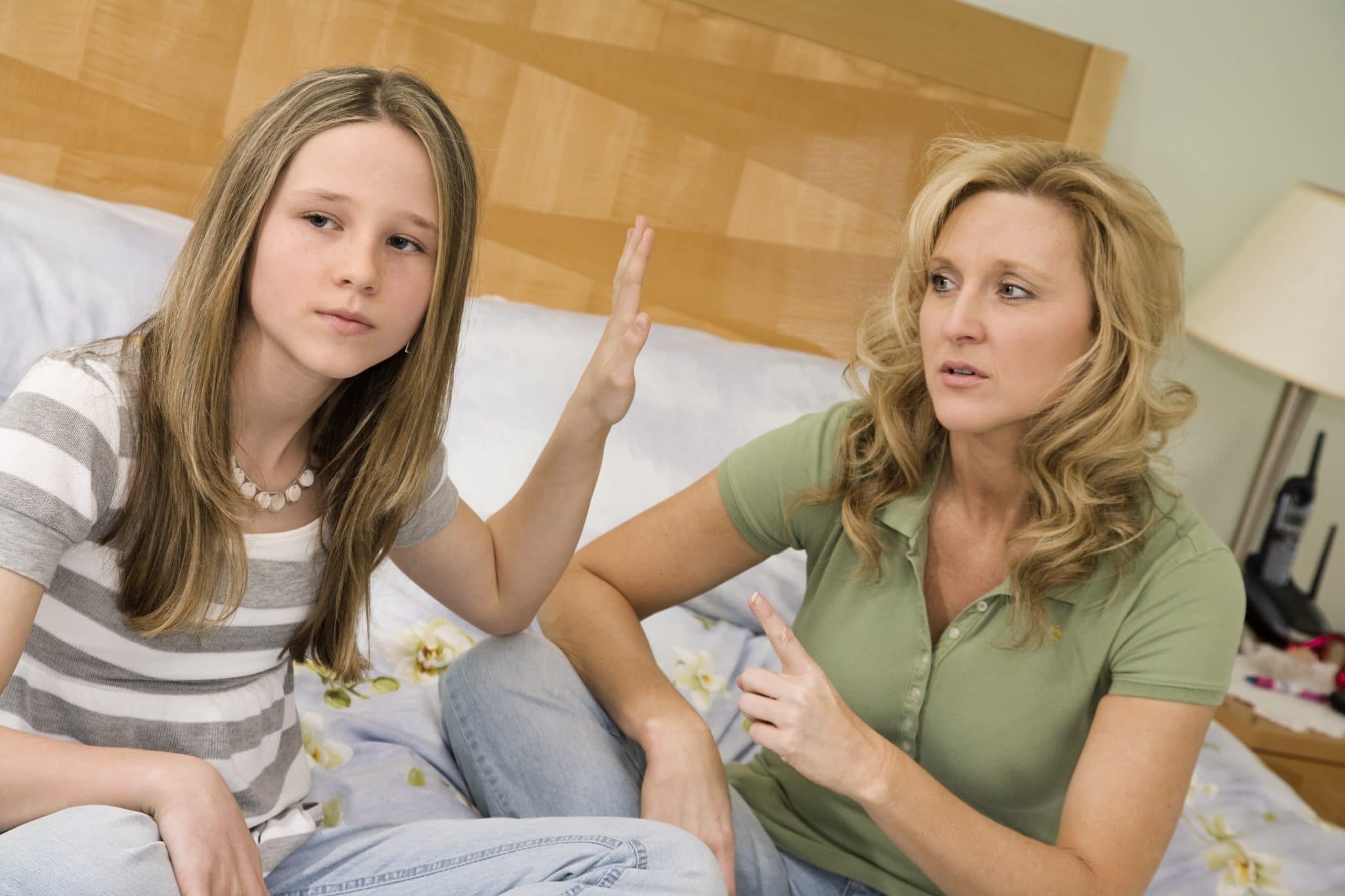 Teen daughter disrespecting mom holding hand in her face.