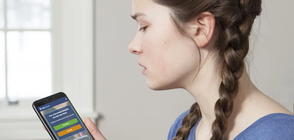 depressed teen Girl holding phone with therapy app shown on screen