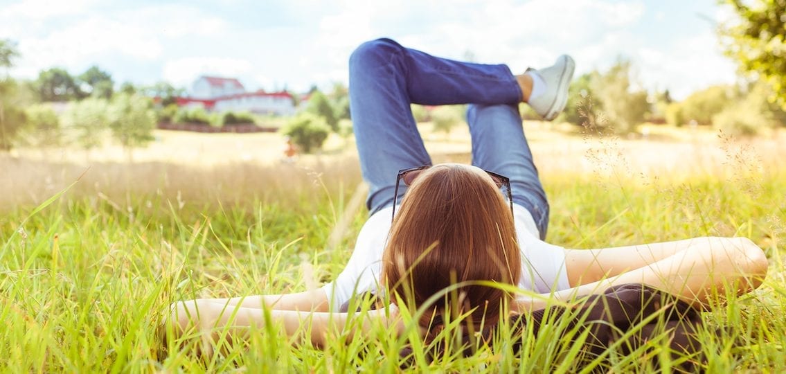 Girl lying alone in the grass hands behind head