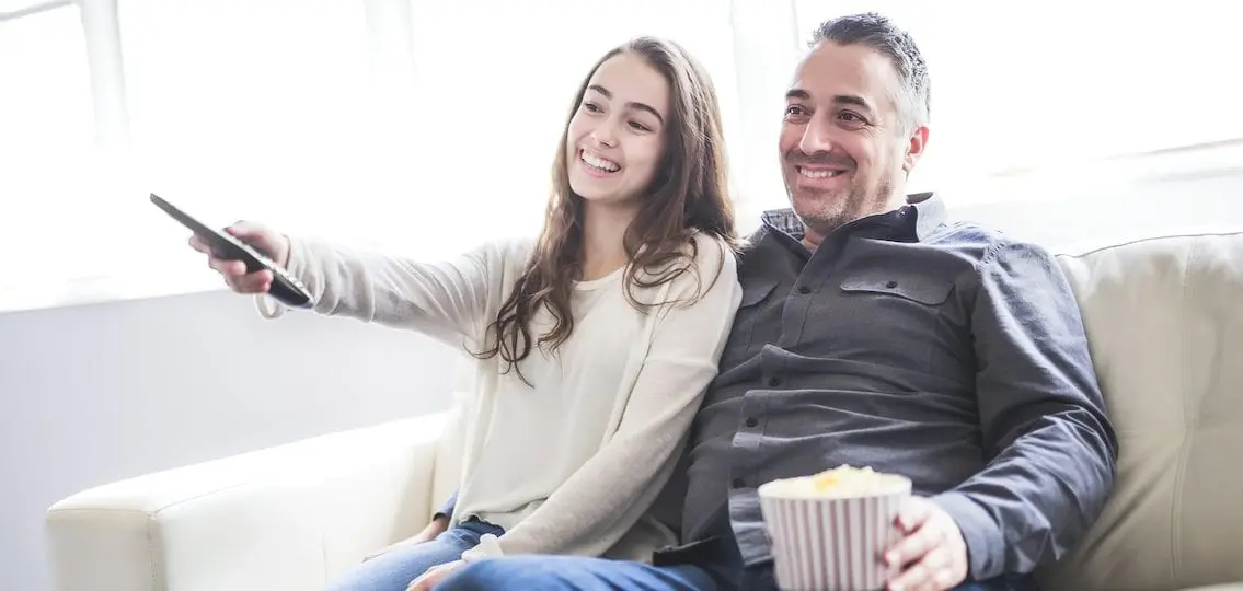 Dad and teen daughter watching TV with popcorn