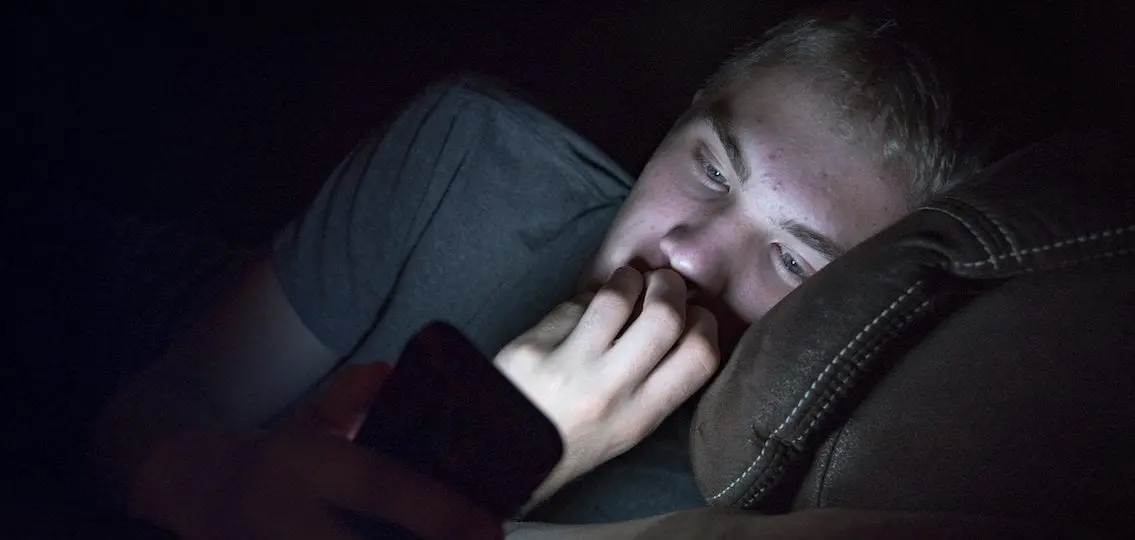 Anxious teen boy texting at night