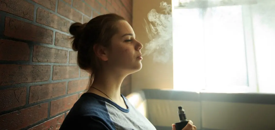 Vaping teenager blowing out smoke in a dimly lit room