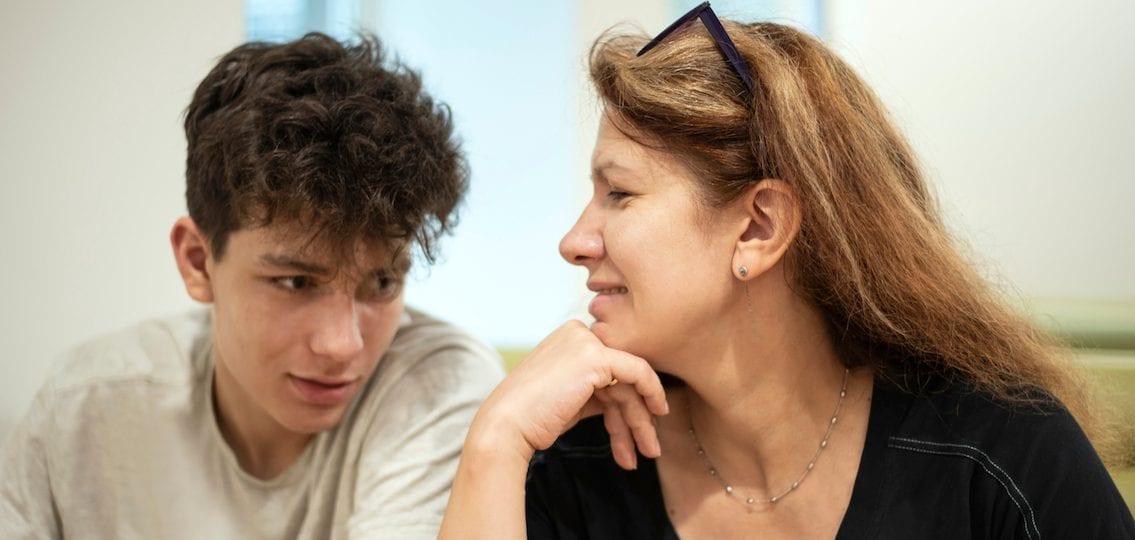 Mom speaking to autistic son who is looking down away from her face