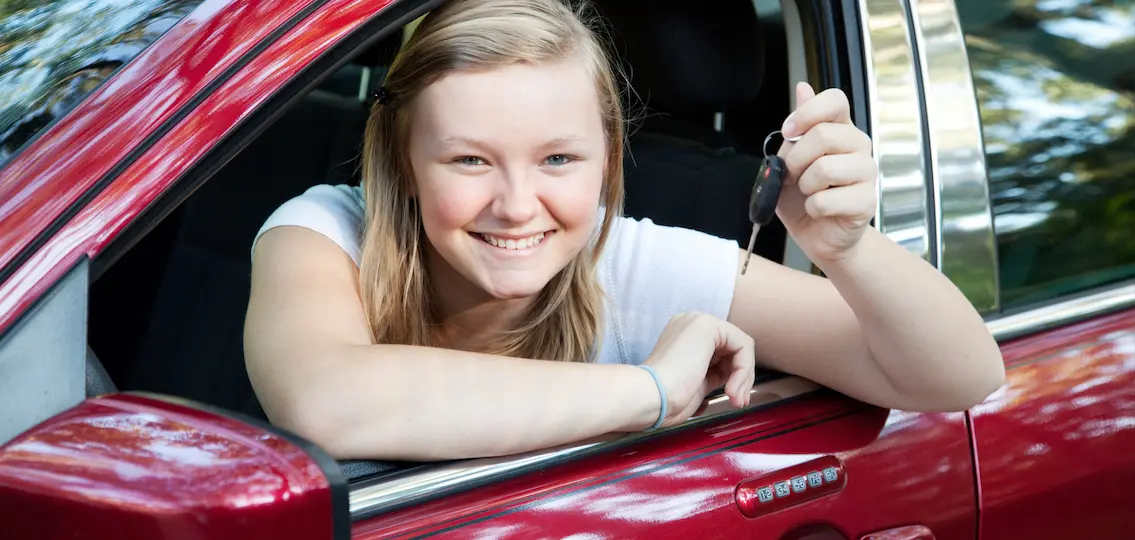 Beautiful blond teenage girl sitting in her new car, holding the keys.
