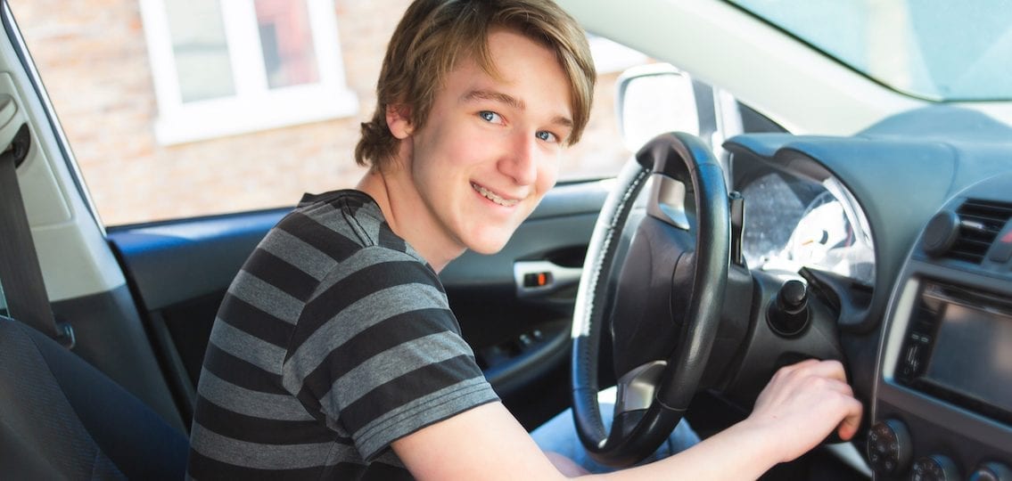 Teen turning on car and smiling from driver's seat