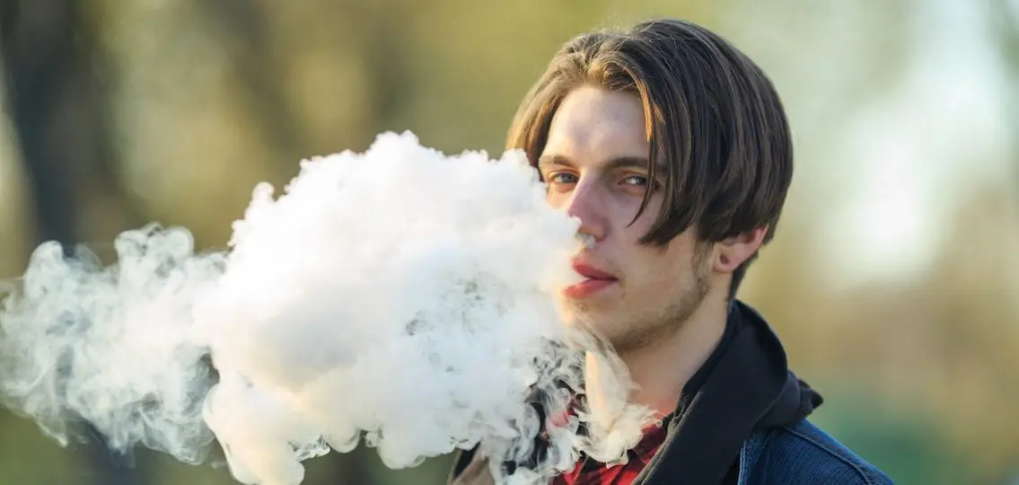 Older teen blowing vape smoke outdoors