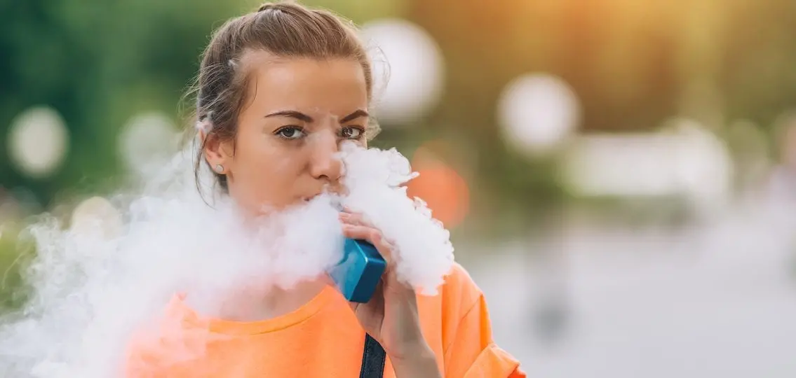 Teen girl vaping outdoors face surrounded by vape smoke