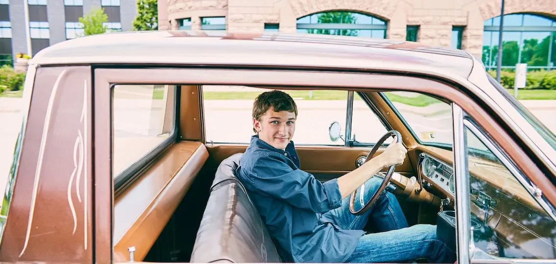 Teenage boy behind the wheel of an old car