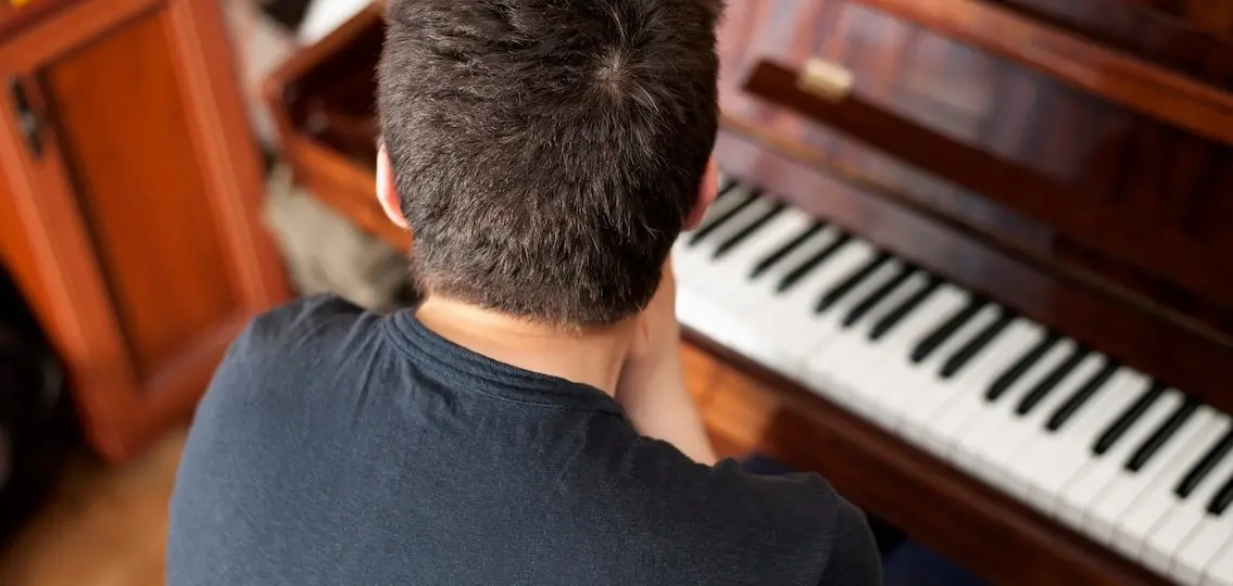 Teen boy at piano facing away from camera