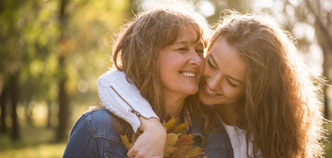 Mom and teen daughter hugging outdoors in autumn