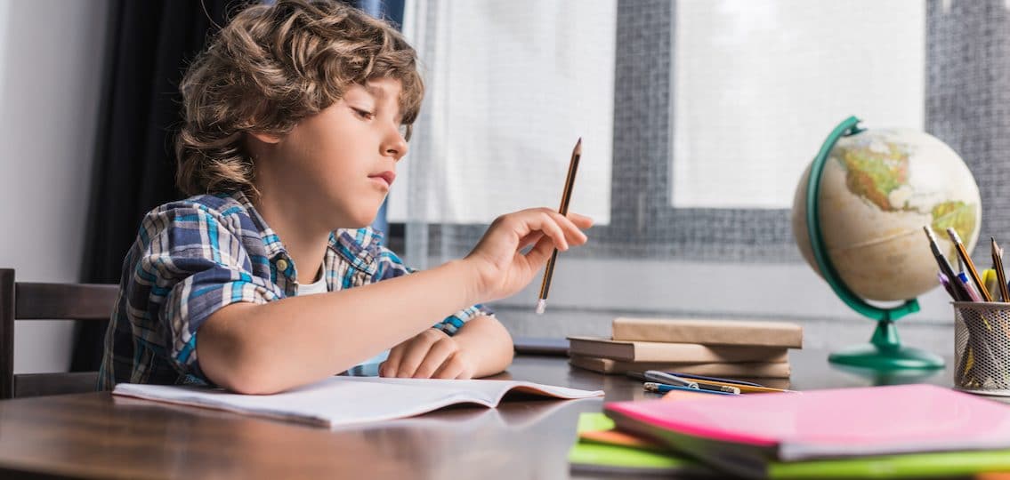 Young boy doing his homework in middle school distracted with pencil