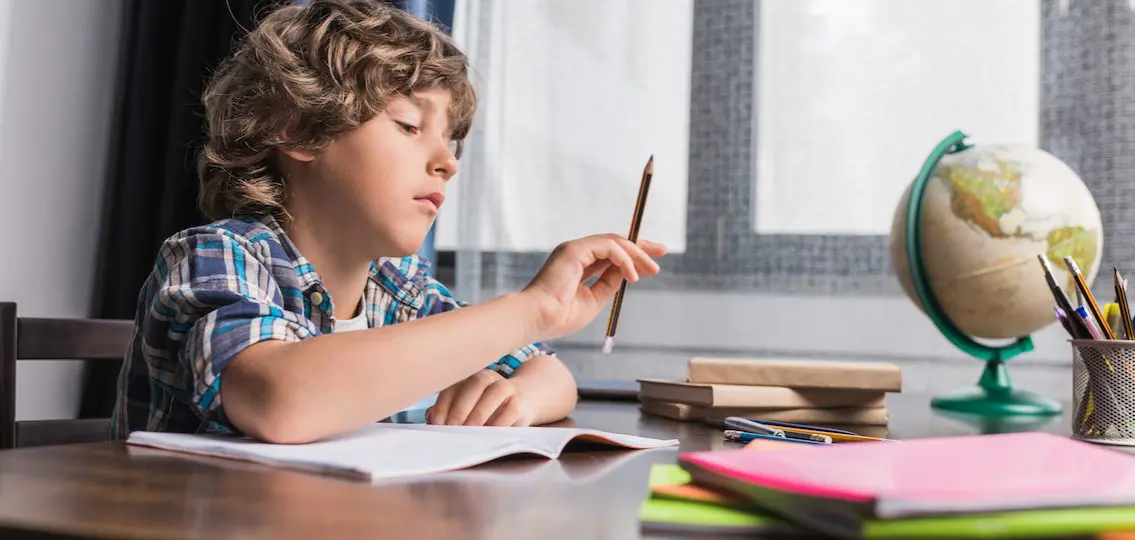 Young boy doing his homework in middle school distracted with pencil