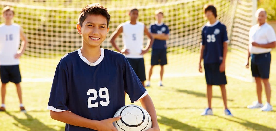 Young JV soccer player with team in background on soccer field