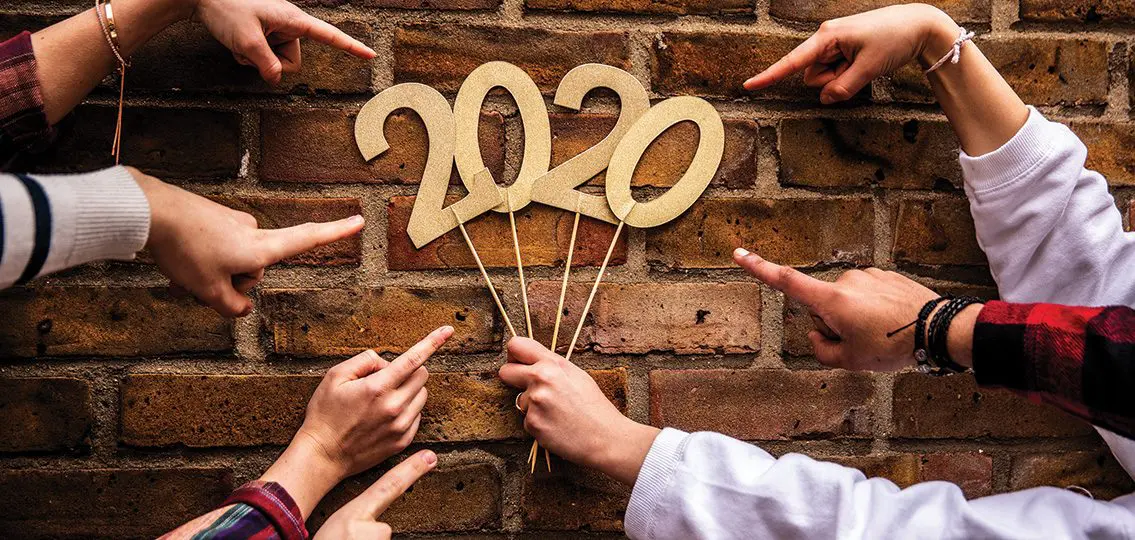 Friends celebrating new year's eve pointing at 2020 sign