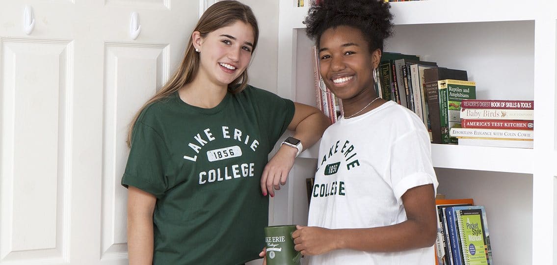 girls in lake erie college shirts standing in front of a white bookshelf