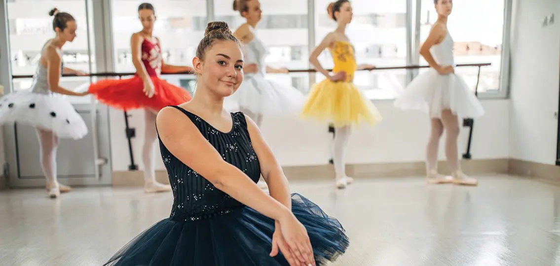 teenage girl in ballet tutu while girls practice ballet in the background