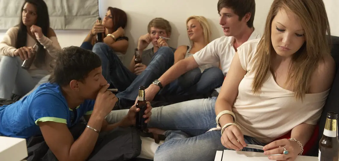 Teenagers drinking and smoking while hanging out one girl rolling a joint