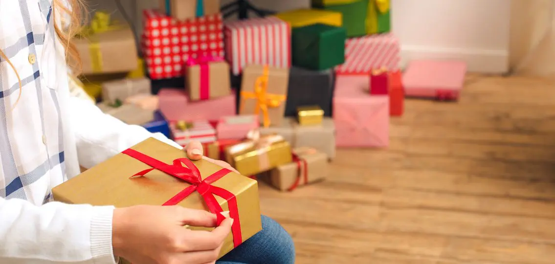 Teen girl opening presents from under christmas tree
