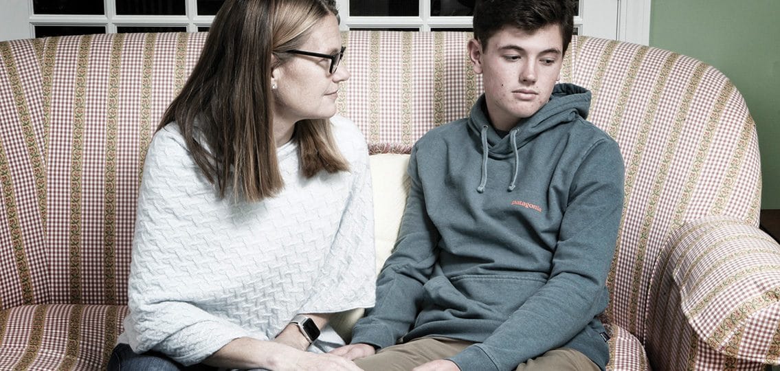 depressed teenage boy on couch being comforted by mother