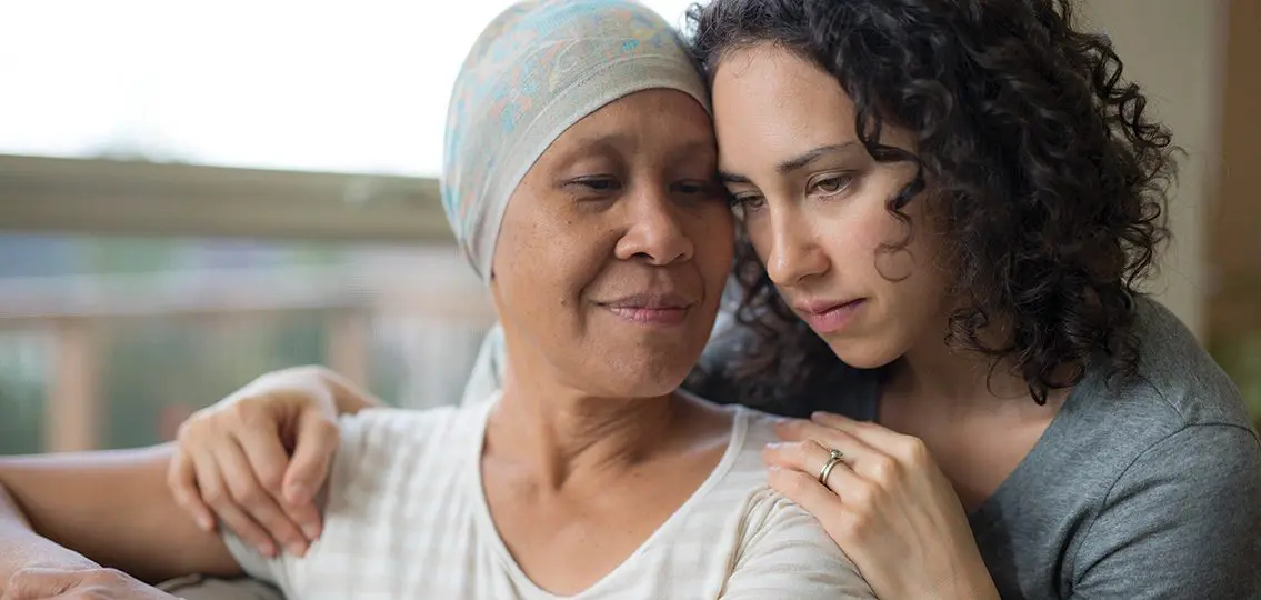 teenage girl hugging her mother who has cancer and is wearing a hat
